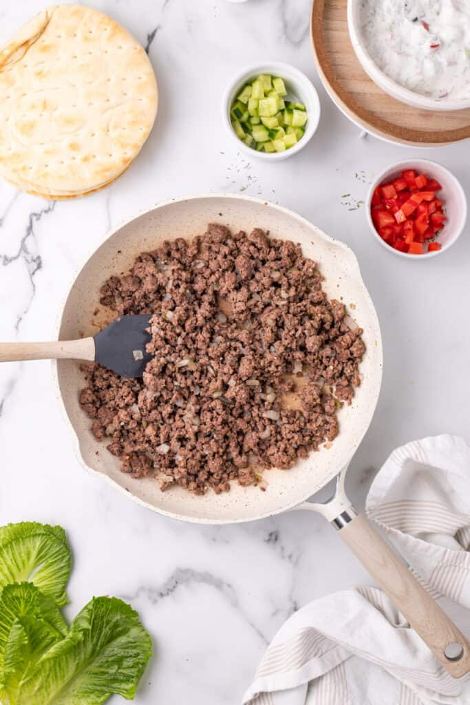 cooked ground beef and onions in a skillet with spatula on a marble surface