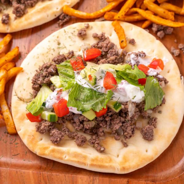 pita breads topped with ground beef, yogurt sauce, cucumber, tomato, and lettuce on a wooden tray