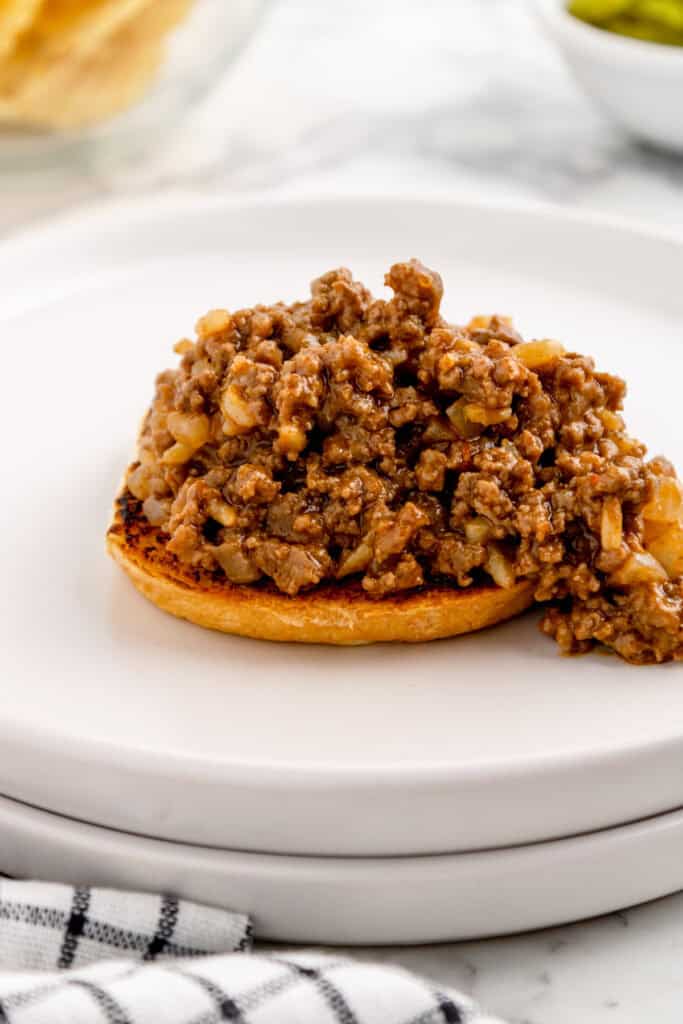 sloppy joe filling piled on the bottom half of a toasted hamburger bun on a white plate