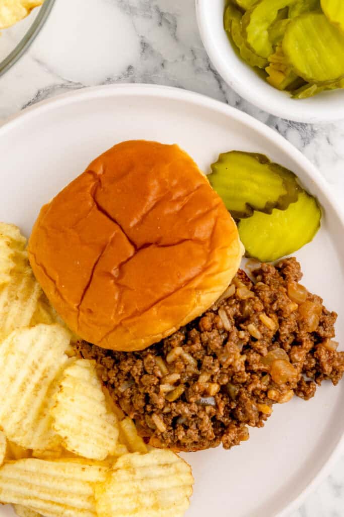 gumbo sloppy joe sandwich served with potato chips and pickle slices on a white plate