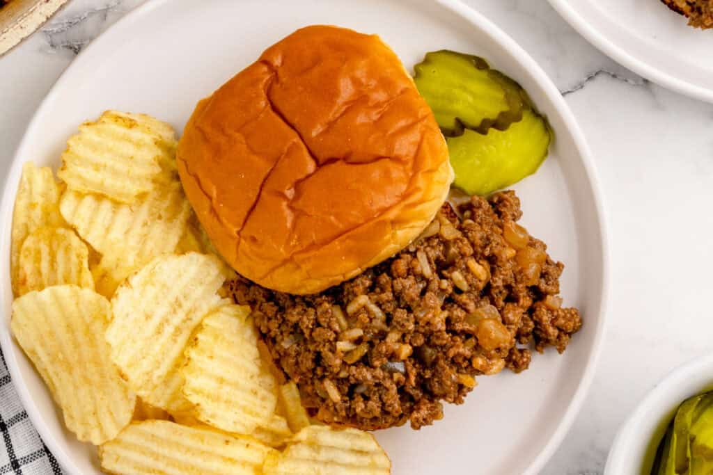 close-up of gumbo sloppy joe sandwich with chips and pickles on a plate