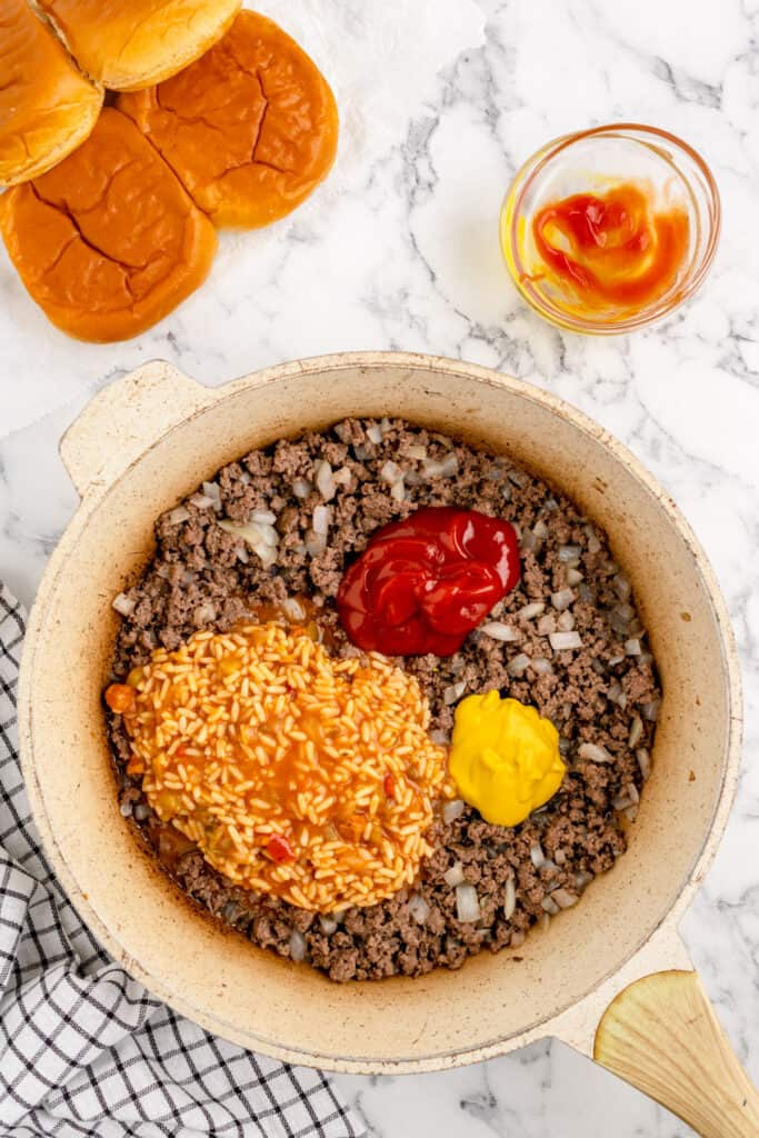 skillet with cooked ground beef and onions topped with ketchup, mustard, and gumbo soup before mixing