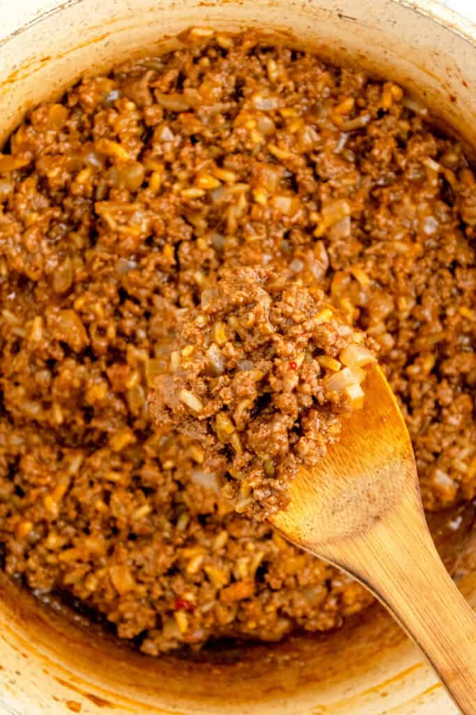 close-up of thick gumbo sloppy joe mixture on a wooden spoon over a skillet