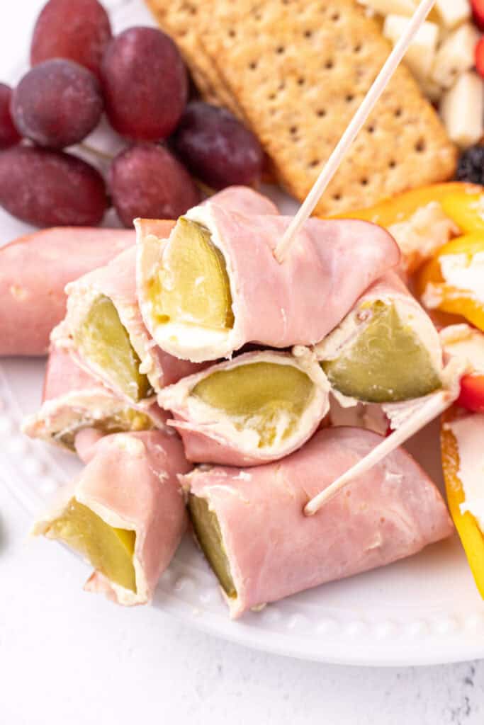 Ham And Pickle Roll-Ups stacked on a plate with toothpicks showing pickle and cream cheese filling