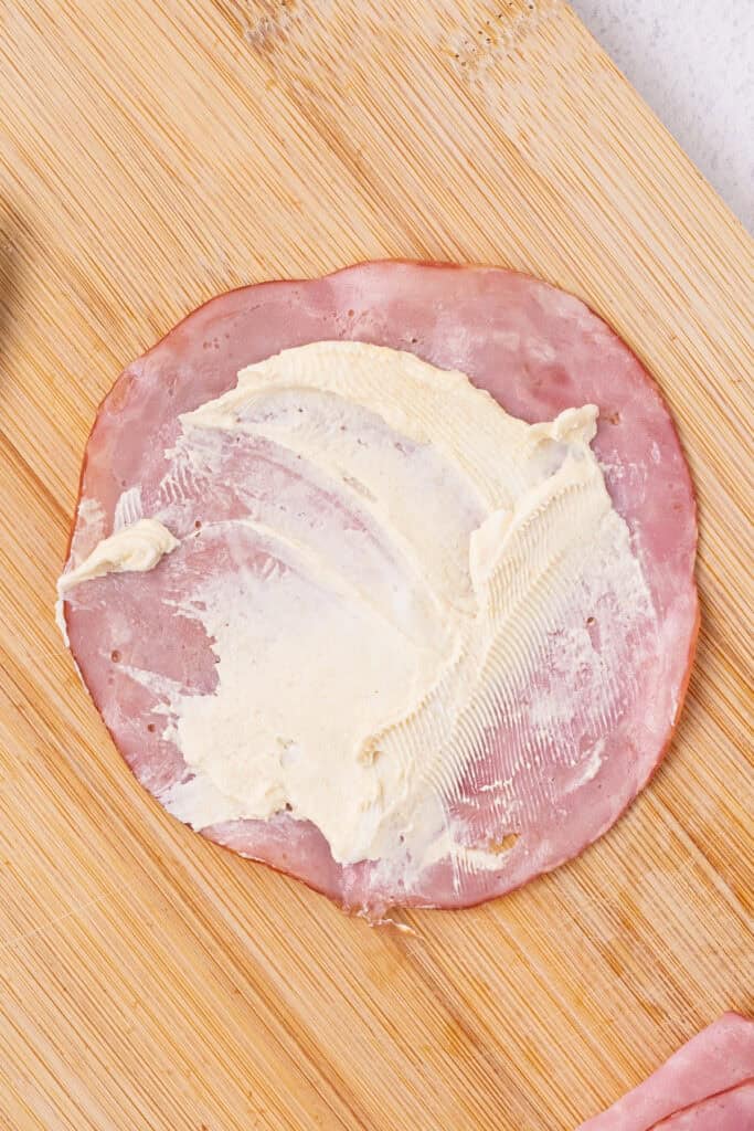 ham slice spread with cream cheese mixture on a cutting board
