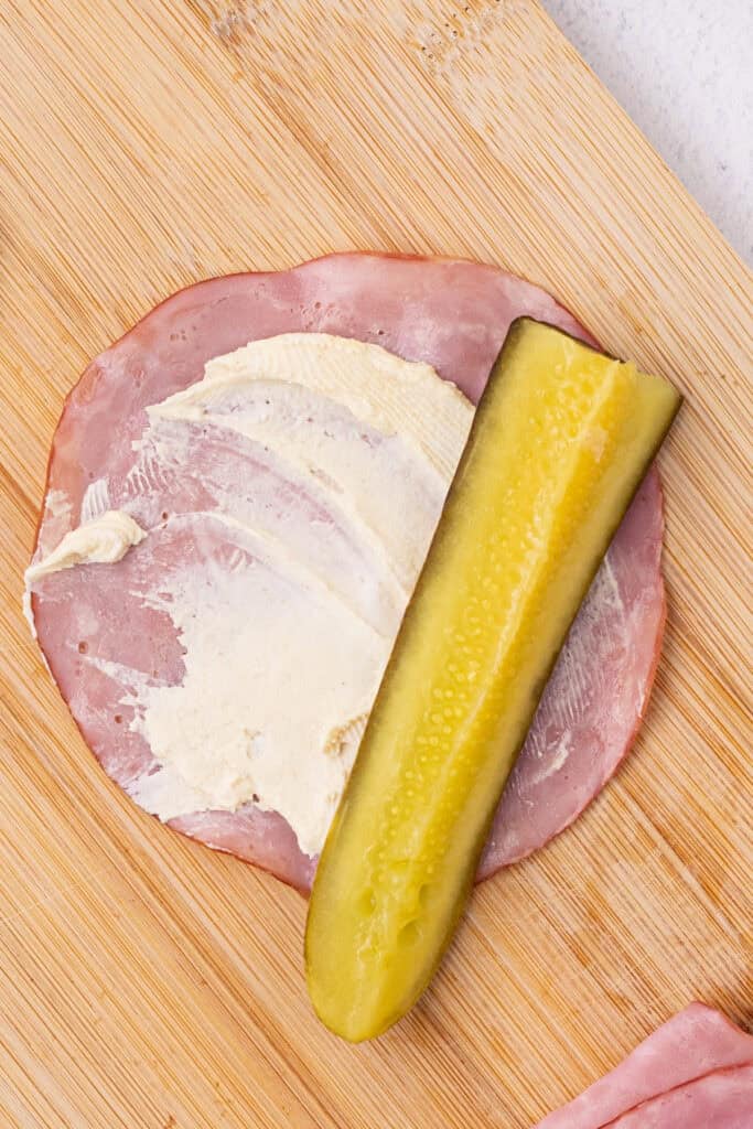 pickle spear placed on top of cream cheese spread on ham slice