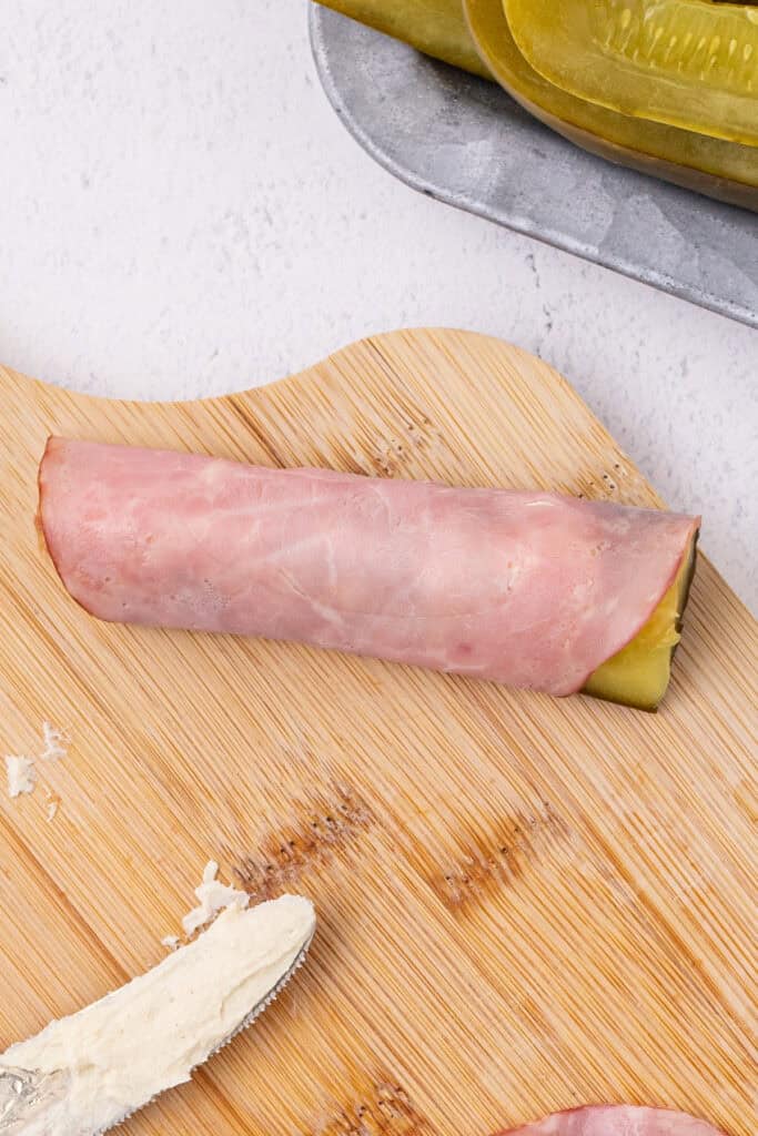 ham rolled around a pickle spear on a cutting board