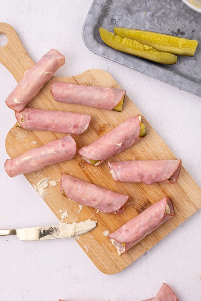 several Ham And Pickle Roll-Ups assembled on a wooden cutting board