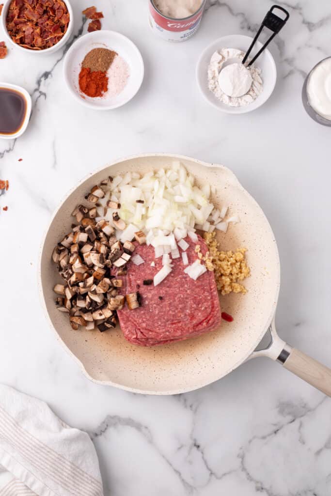 raw ground beef with chopped mushrooms, diced onion, and minced garlic added to a skillet for hamburger stroganoff sloppy joes