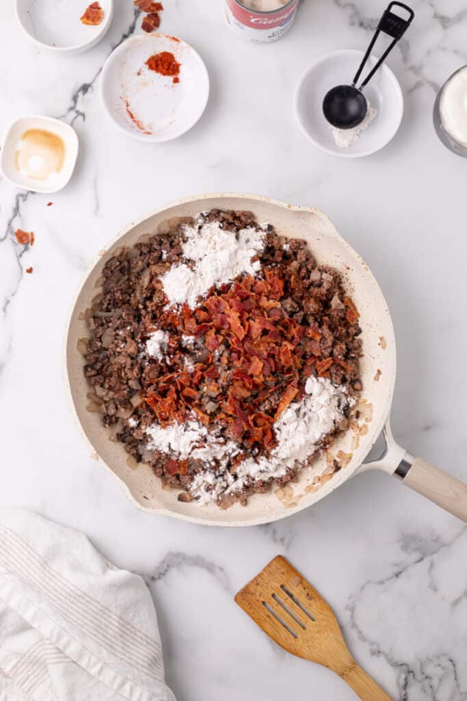 cooked ground beef mixture topped with bacon, flour, and spices in a skillet for hamburger stroganoff sloppy joes