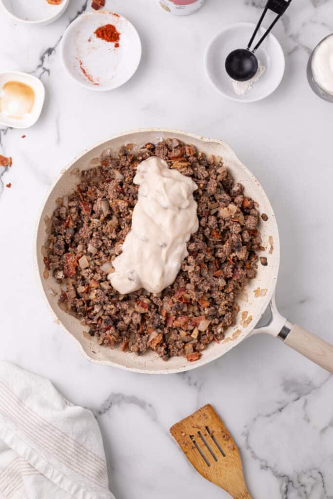cream of mushroom soup added to cooked ground beef mixture in a skillet for hamburger stroganoff sloppy joes