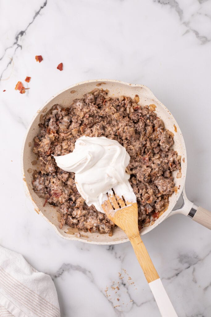 sour cream being added to creamy beef mixture in a skillet for hamburger stroganoff sloppy joes