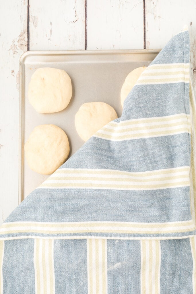 homemade onion rolls dough on a baking sheet covered with a kitchen towel for rising
