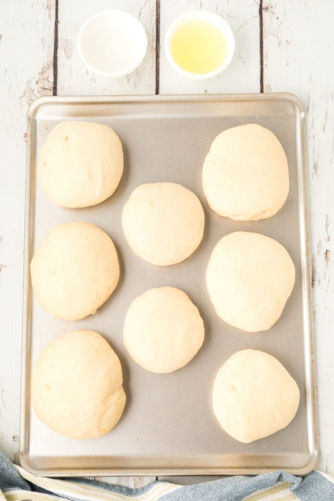 risen homemade onion rolls dough on a baking sheet with egg wash and a small bowl of egg mixture