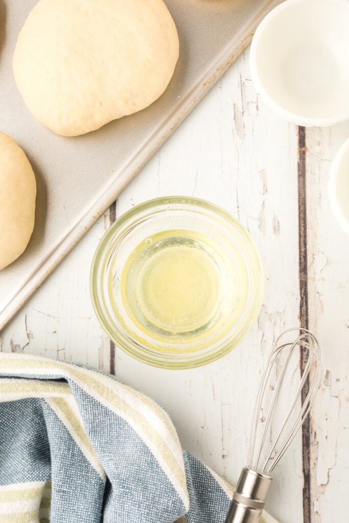 egg wash in a small bowl with a whisk next to homemade onion rolls dough on a baking sheet