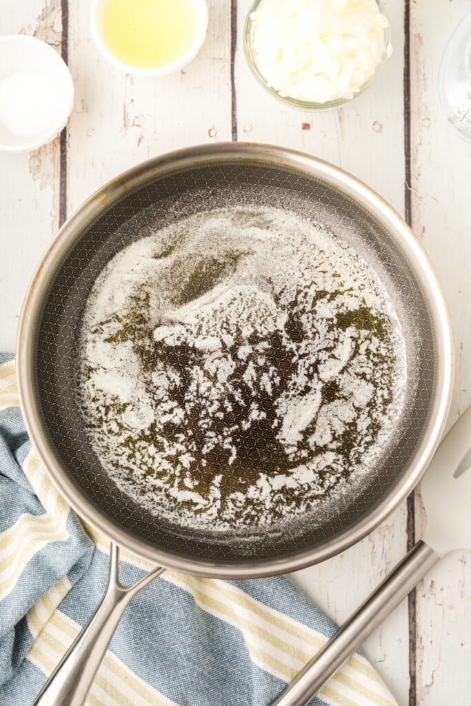melted butter in a skillet with chopped onion and ingredients nearby on a white wooden surface