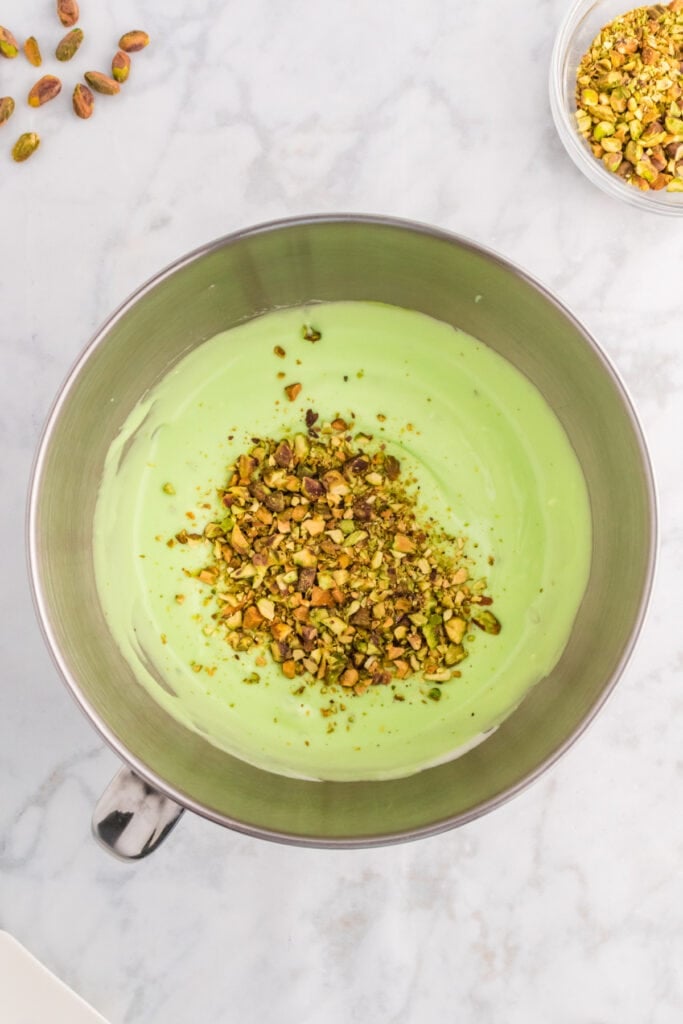 chopped pistachios added to green pistachio filling mixture in a mixing bowl