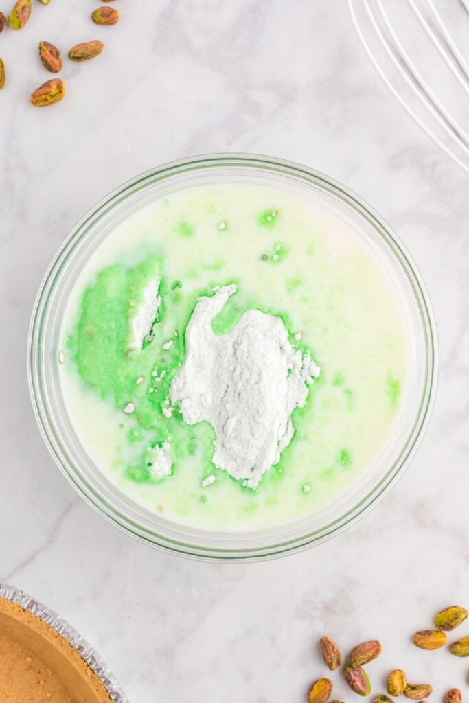 bowl with milk, pistachio pudding mix, and green food coloring beginning to combine