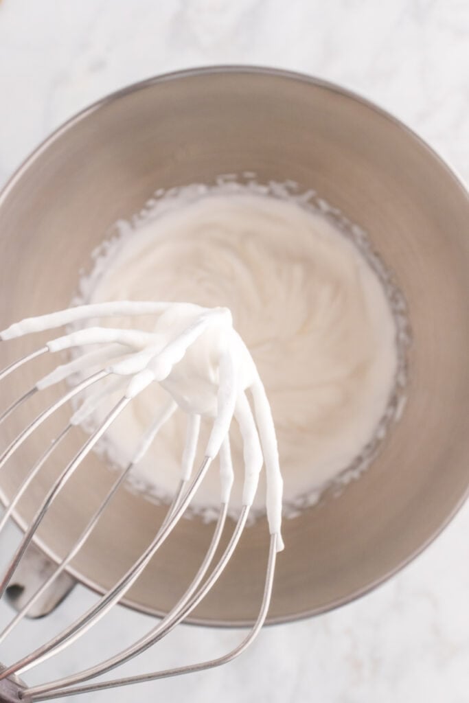 whisk attachment with whipped cream forming soft peaks in a mixing bowl