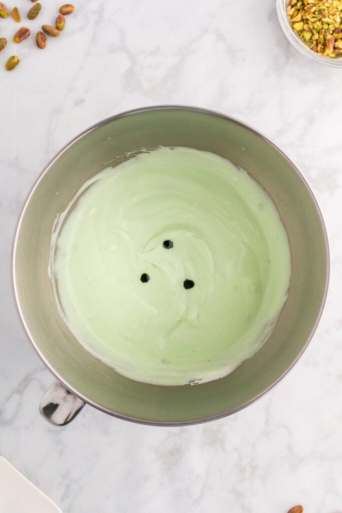 green pistachio filling mixture with drops of food coloring in a mixing bowl