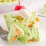 square image of pistachio cream pie slice with whipped cream and cherry on top