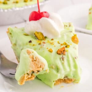 square image of pistachio cream pie slice with whipped cream and cherry on top