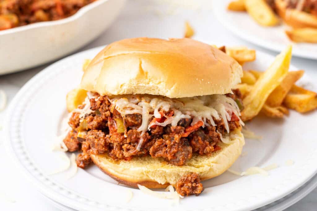 Pizza Sloppy Joes sandwich with melted mozzarella on a hamburger bun served with fries on a white plate