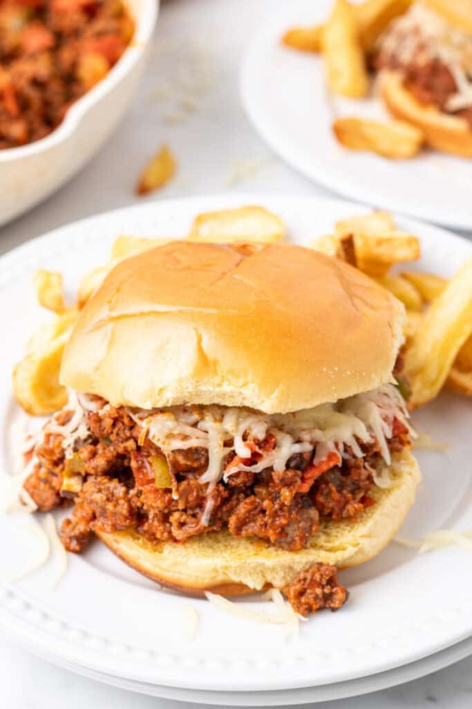 close up of Pizza Sloppy Joes sandwich with melted mozzarella on a hamburger bun served with fries on a white plate