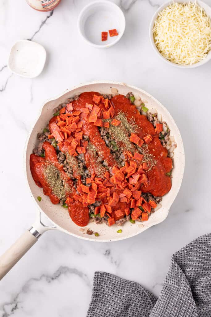 ground beef mixture topped with pizza sauce, chopped pepperoni, and oregano in a skillet for Pizza Sloppy Joes