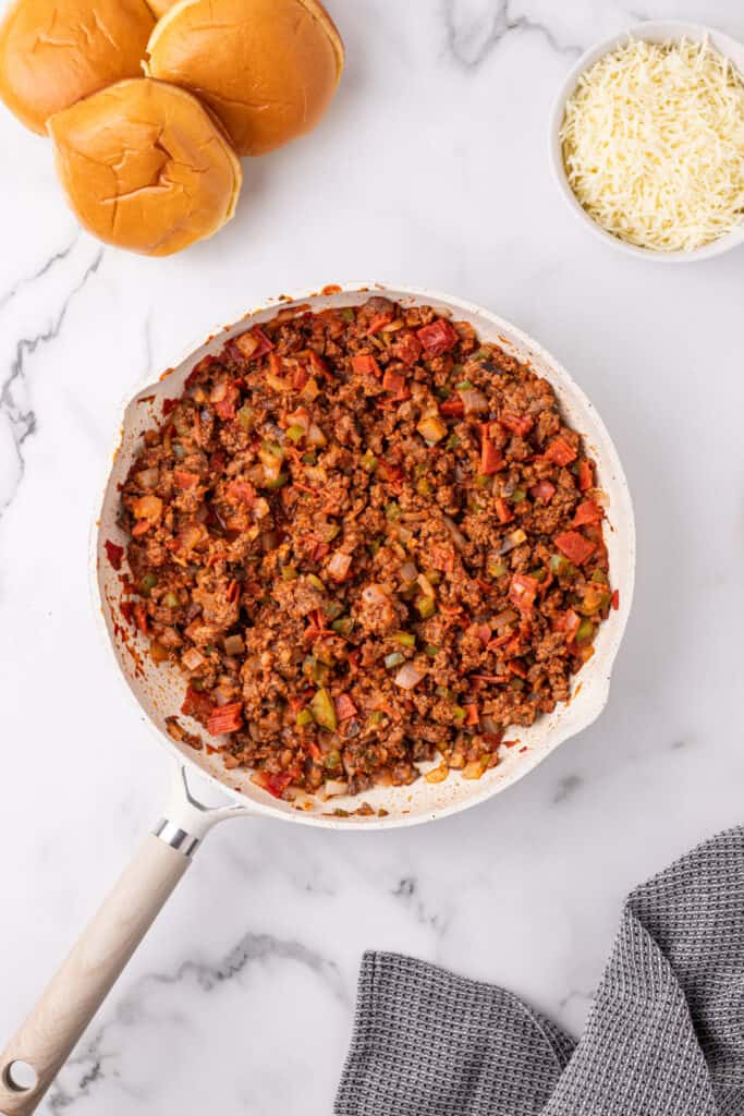 fully cooked Pizza Sloppy Joes meat mixture in a skillet with hamburger buns and shredded cheese nearby