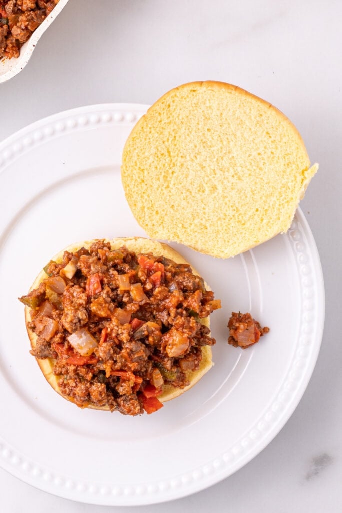 Pizza Sloppy Joes meat mixture spooned onto the bottom half of a hamburger bun on a white plate