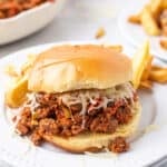 Pizza Sloppy Joes sandwich with melted mozzarella on a hamburger bun served with fries on a white plate