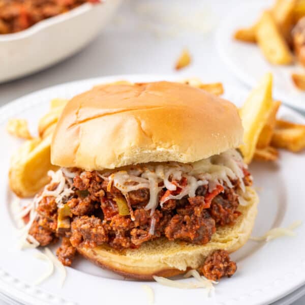 Pizza Sloppy Joes sandwich with melted mozzarella on a hamburger bun served with fries on a white plate