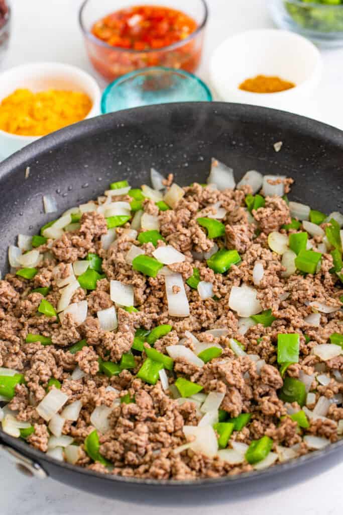 ground beef cooking in a skillet with diced onion and green bell pepper for Taco Sloppy Joes
