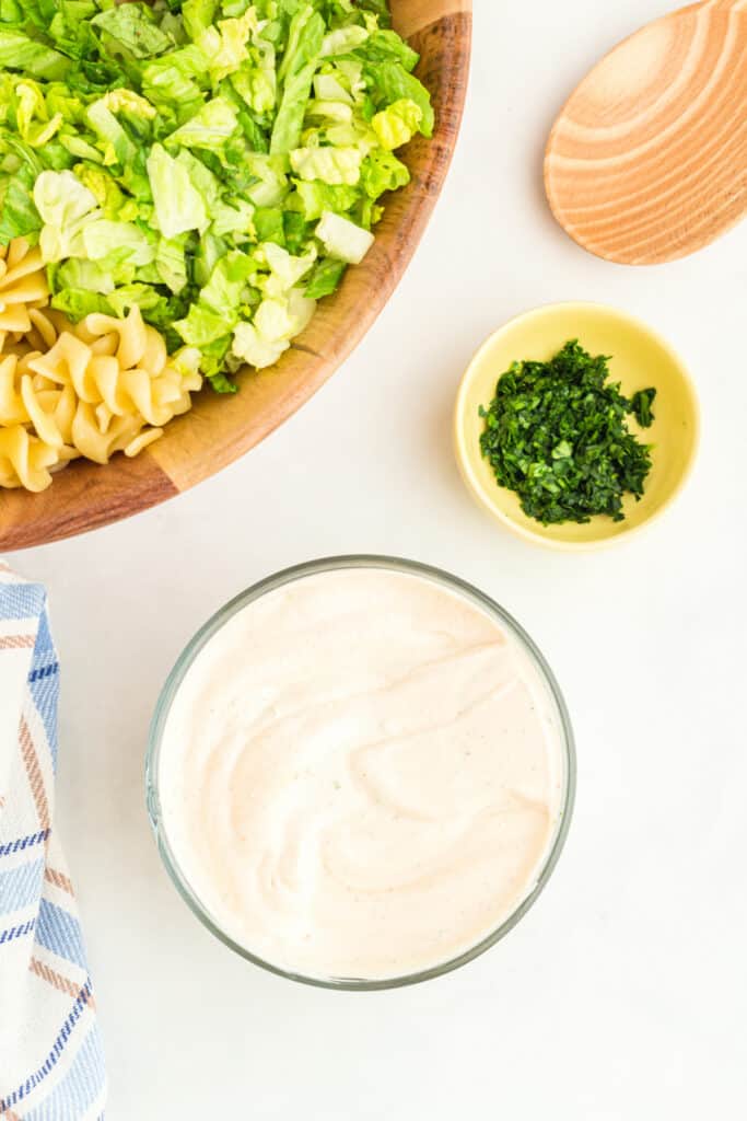 close up of shredded romaine lettuce and rotini pasta in a bowl with chopped parsley and BBQ ranch dressing nearby