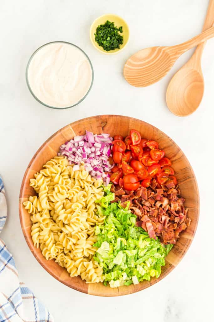 rotini pasta, diced red onion, cherry tomatoes, chopped bacon, and shredded lettuce arranged in a wooden bowl for BBQ Ranch BLT Pasta Salad