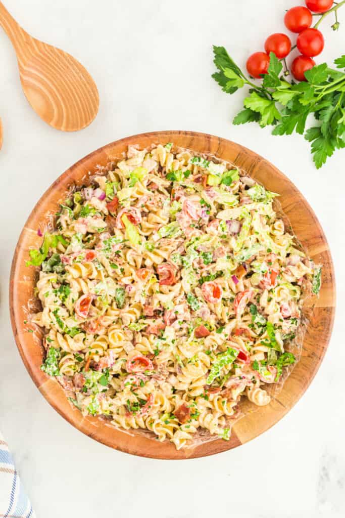 BBQ ranch dressing in a glass bowl with parsley and wooden spoons next to a bowl of pasta salad ingredients