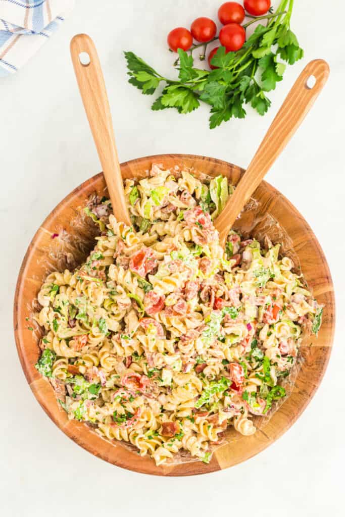 overhead view of BBQ Ranch BLT Pasta Salad in a wooden bowl with fresh parsley and cherry tomatoes on the side