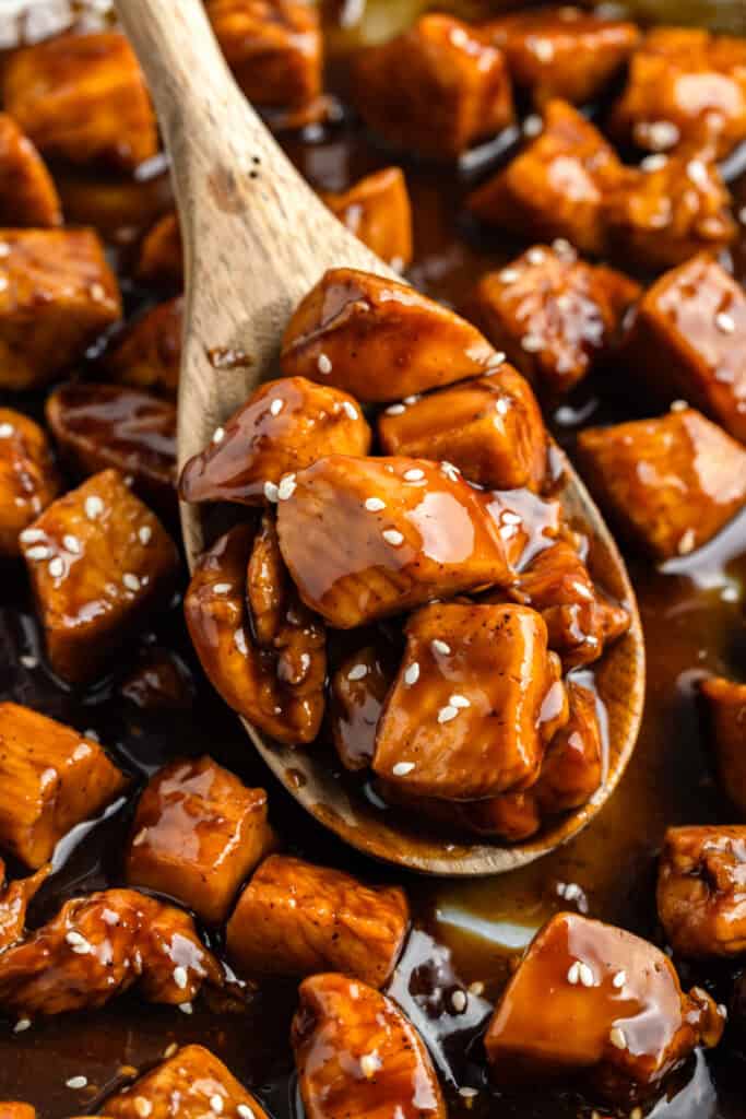 Wooden spoon holding saucy Chicken Teriyaki pieces with sesame seeds