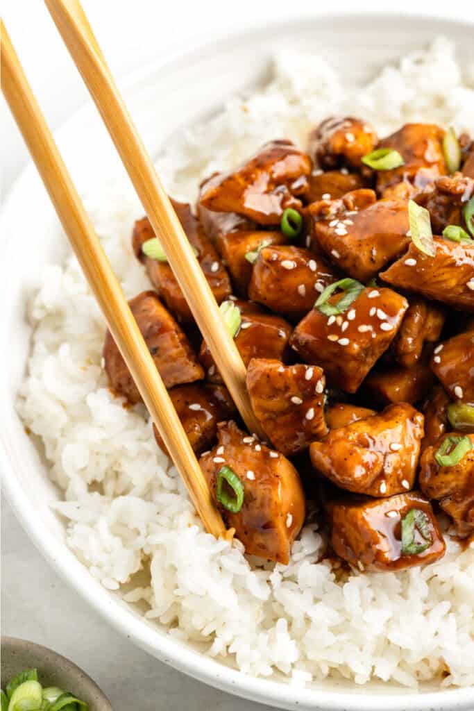 Chicken Teriyaki rice bowl with chopsticks, sesame seeds, and sliced green onions