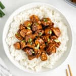 Chicken Teriyaki served over white rice with sesame seeds and sliced green onions in a white bowl