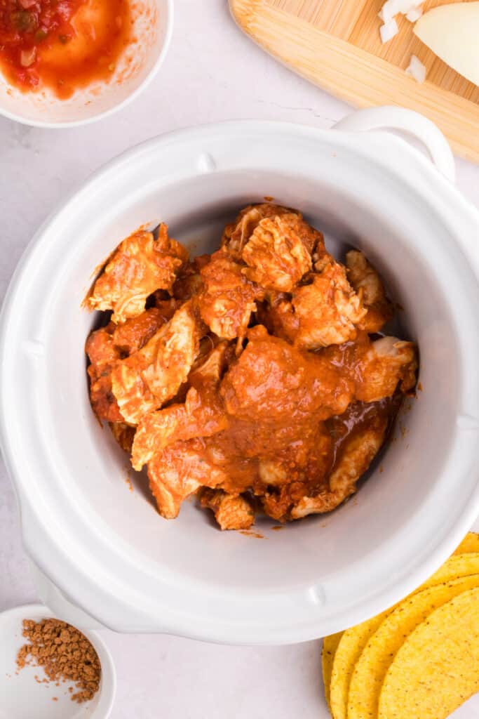 Cooked chicken with salsa and taco seasoning in a slow cooker before shredding for Crockpot Shredded Chicken Tacos