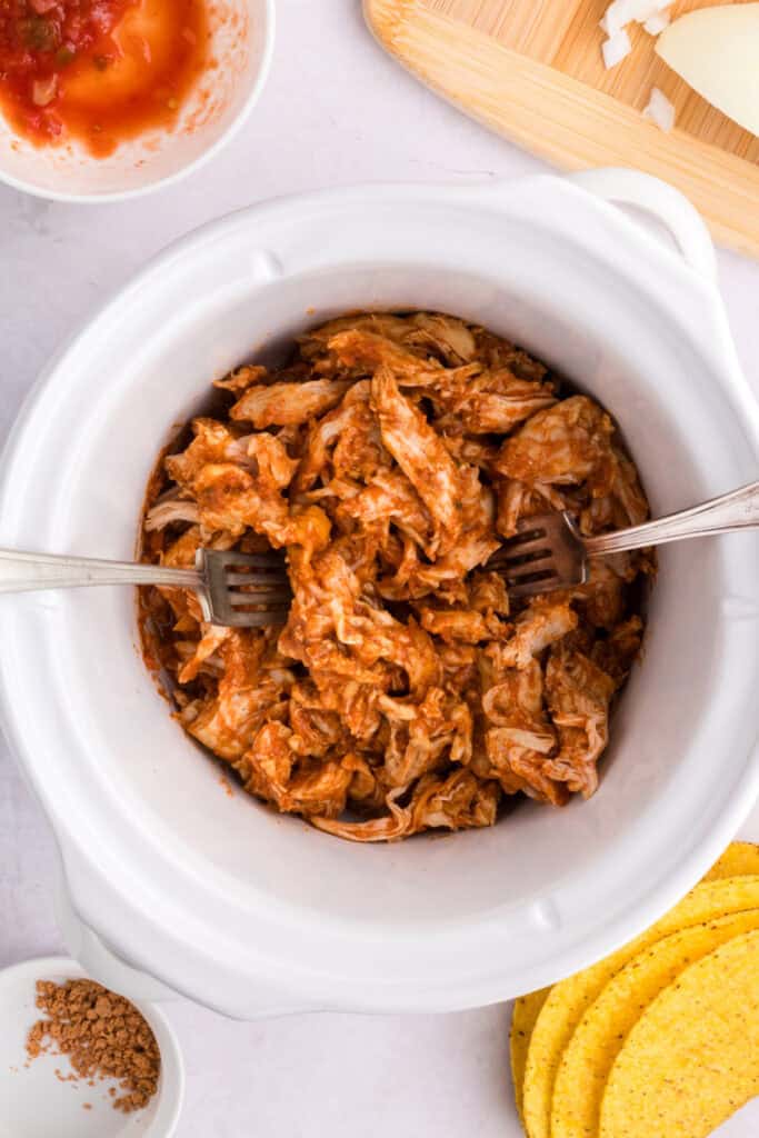Shredded taco chicken mixed in sauce inside a slow cooker for Crockpot Shredded Chicken Tacos