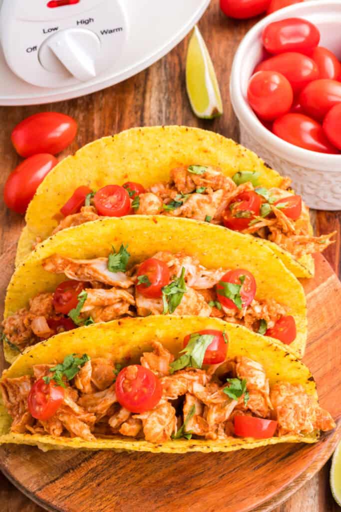 Crockpot Shredded Chicken Tacos topped with chopped tomatoes and cilantro in crispy taco shells