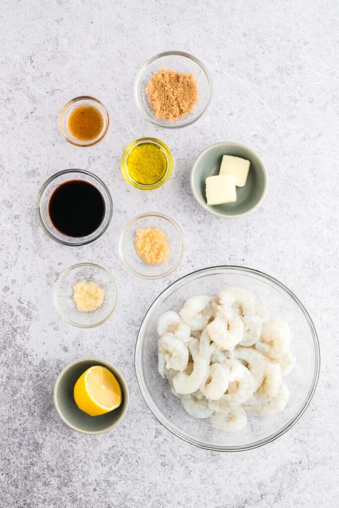 Ingredients for Hibachi Shrimp arranged on a light countertop, including raw shrimp, soy sauce, sesame oil, brown sugar, garlic, ginger, butter, and lemon.