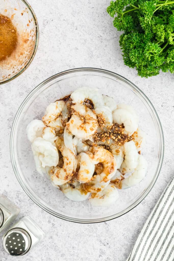 Raw shrimp in a glass bowl topped with Hibachi Shrimp marinade ingredients.