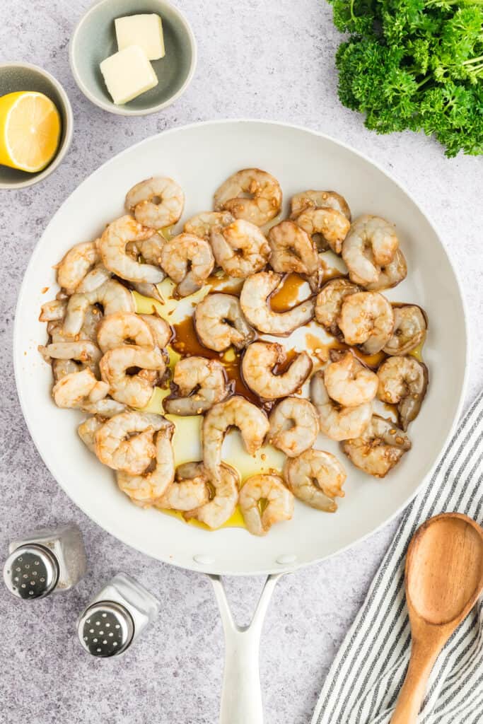 Marinated shrimp and butter added to a white skillet before cooking.