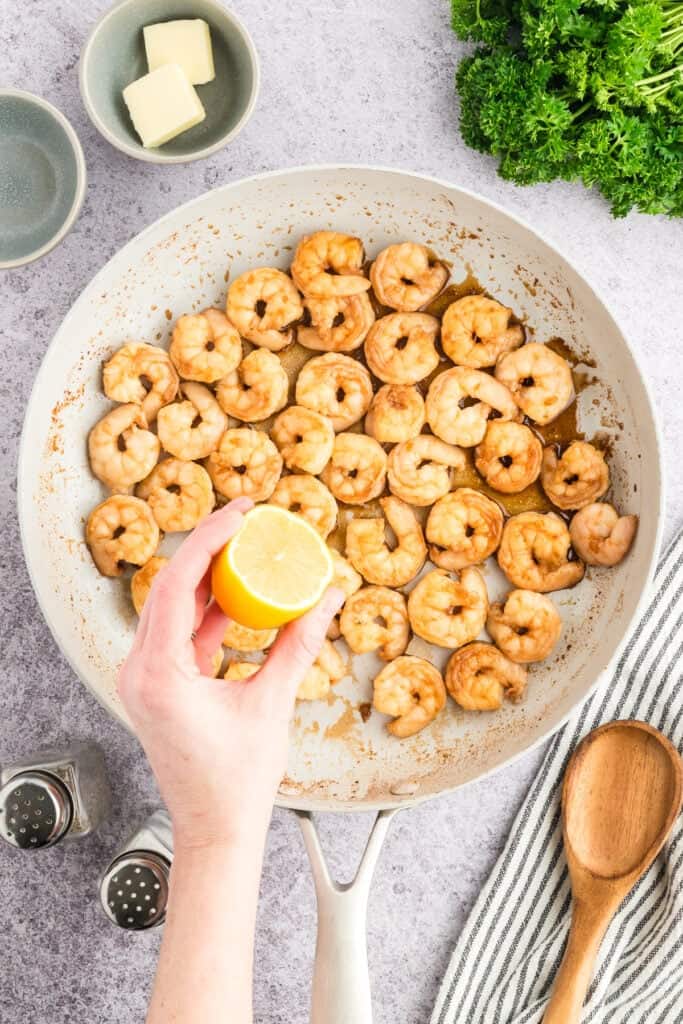 Fresh lemon juice being squeezed over cooked Hibachi Shrimp in a skillet.