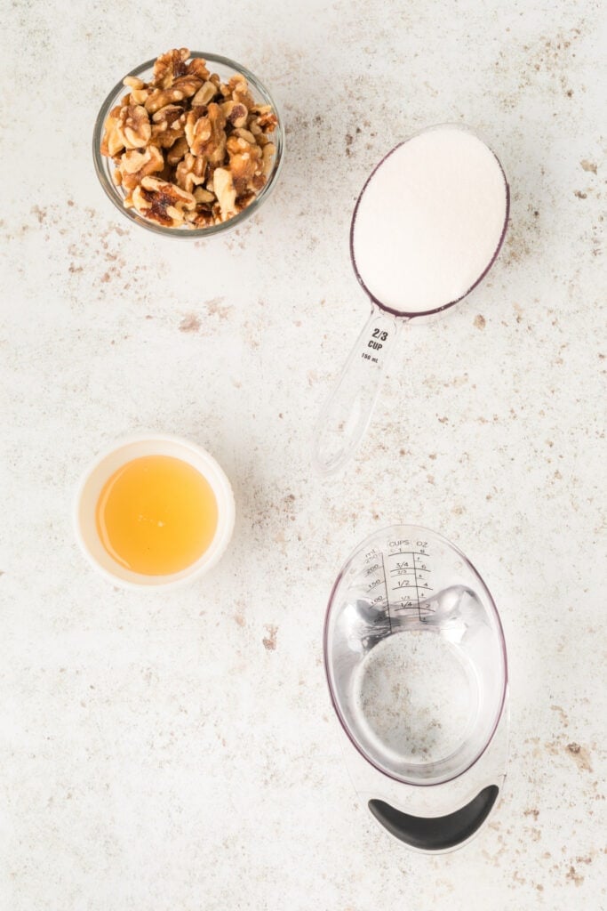Ingredients for Honey Walnut Shrimp including walnuts, granulated sugar, honey, and water on a light background