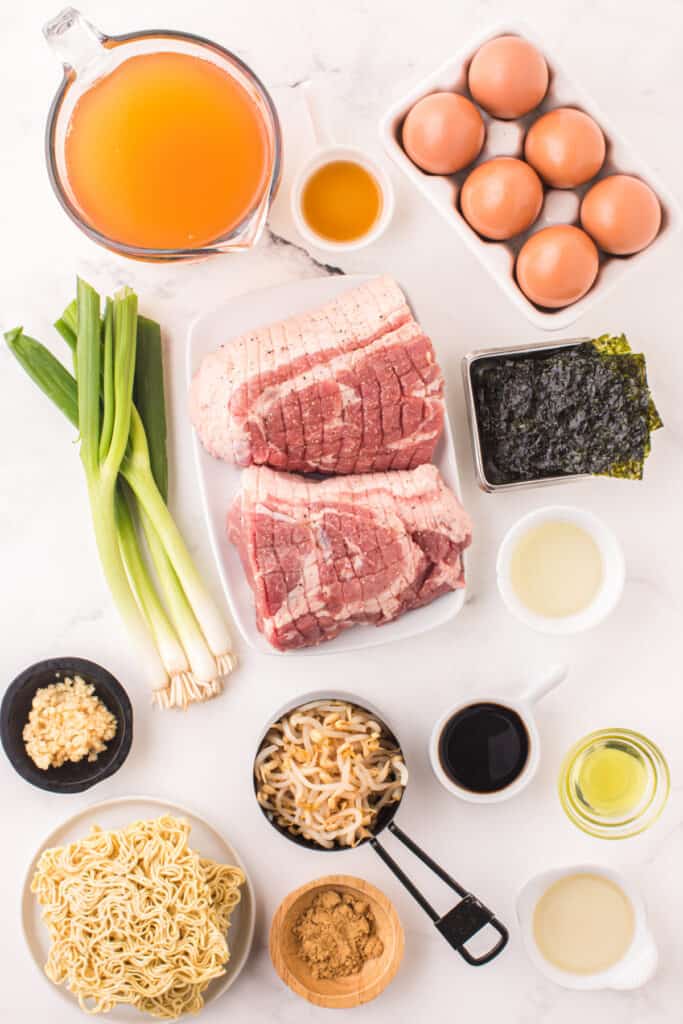 Ingredients for Instant Pot Ramen including pork shoulder, eggs, green onions, ramen noodles, bean sprouts, nori, broth, garlic, and seasonings arranged on a white surface